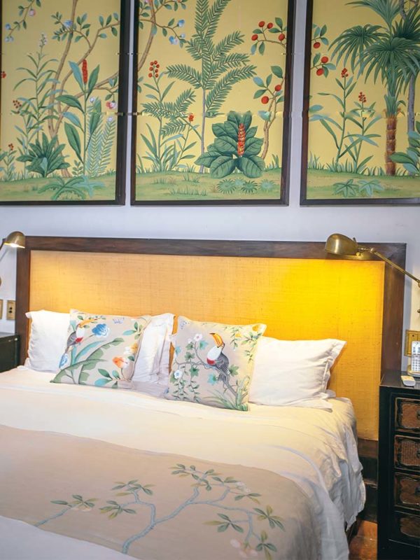 Cama doble con cabecero tapizado en oro en la habitación Toucan con cojines y estampados enmarcados de los pájaros de arriba