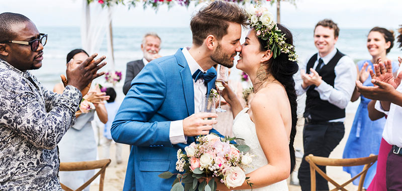 Recién casados besándose mientras están rodeados por sus invitados de bodas en Amarla Cartagena de Indias en la playa